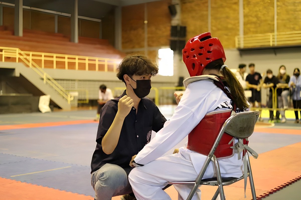 Coach speaking with a young Taekwondo athlete between rounds at a tournament