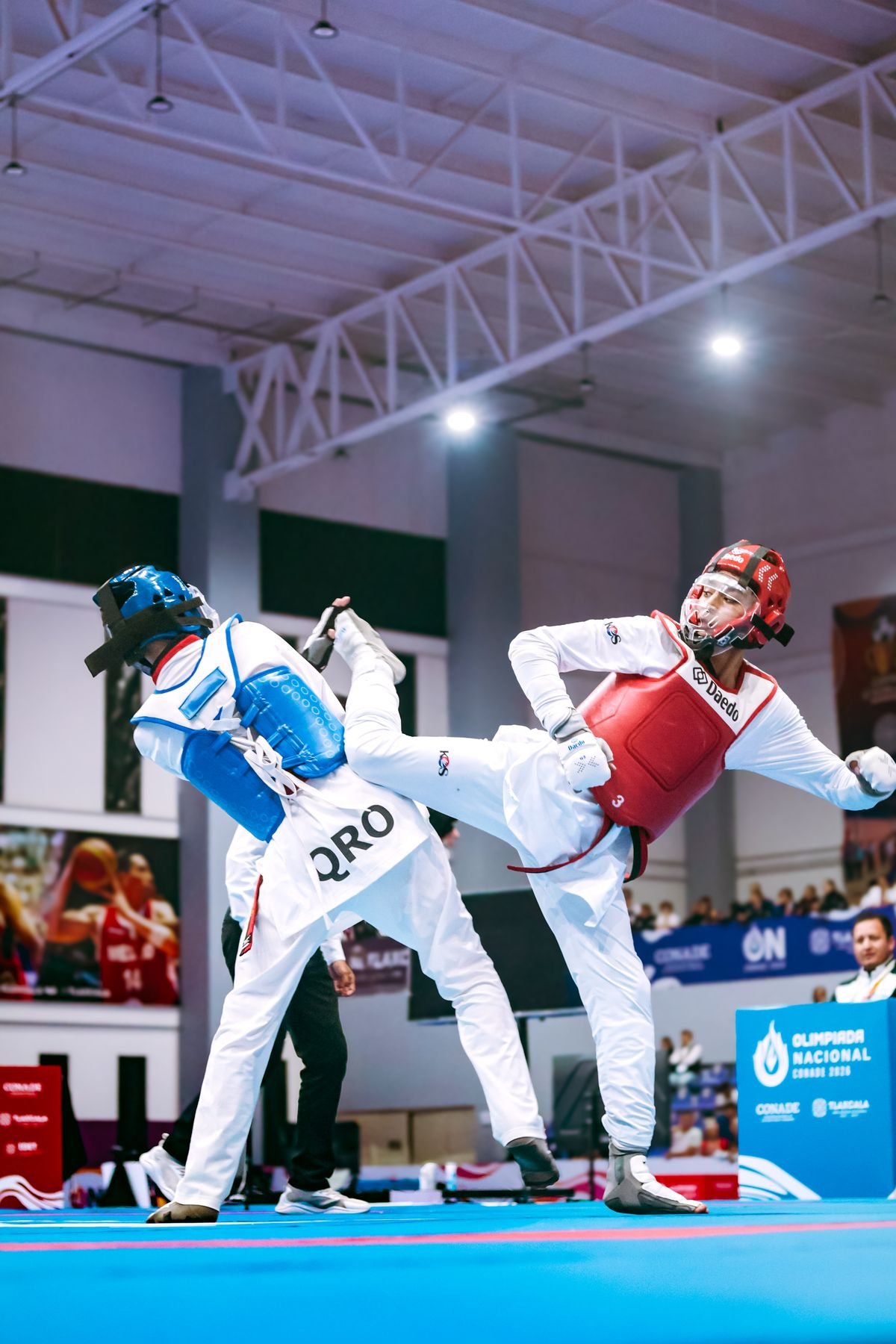 Taekwondo athlete in red hogu landing a side kick during a tournament match